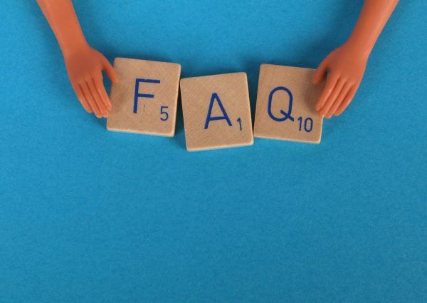 Flat lay of scrabble tiles spelling 'FAQ' with toy hands on a blue background, creating a conceptual image.